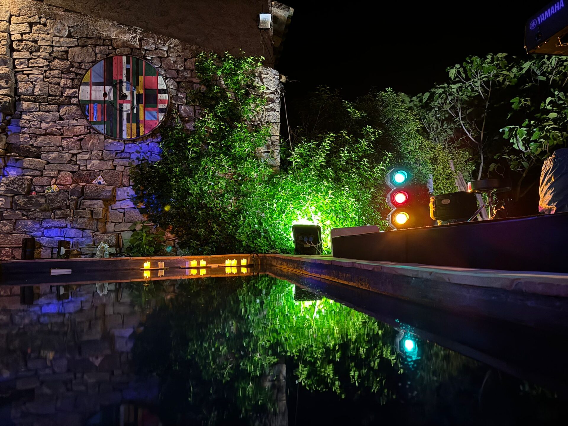Parets de pedra il·luminades per llums acolorides a la nit, reflexos en superfície d'aigua.