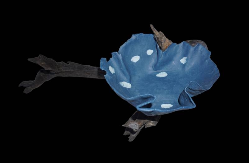 Escultura de porcelana azul con manchas blancas sobre madera oscura.